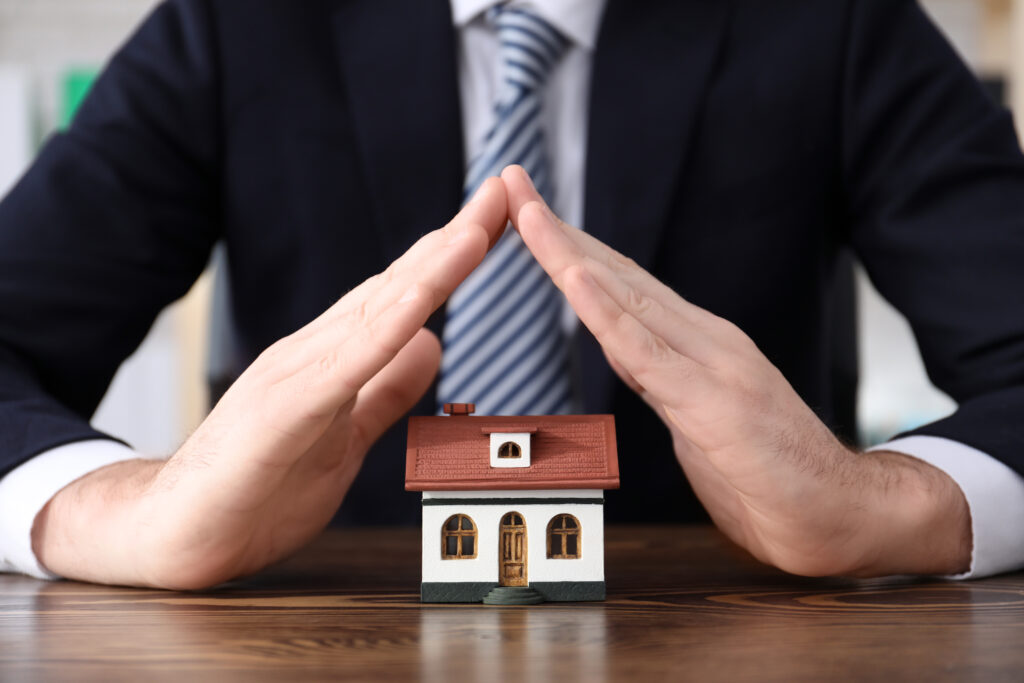 A person protecting a small house model with hands.